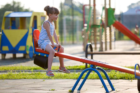 Cute young child girl outdoors on see-saw swing on sunny summer day.の写真素材