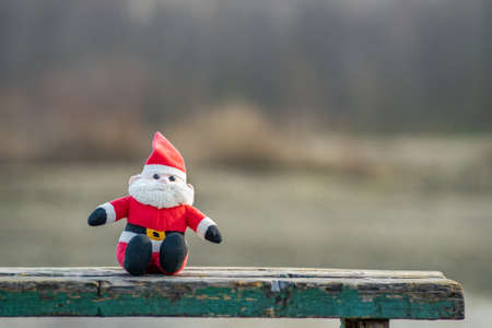 Close up of small santa clause toy on wooden bench outdoors.