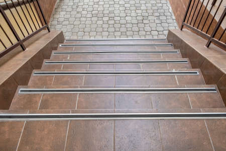 Concrete entrance stairs covered with ceramic tiles with metal railings outdoors.