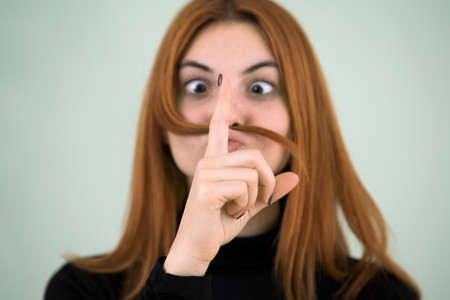 Close up portrait of funny girl holding long red hair like a mustache under her nose.