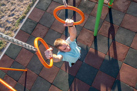 Young fit athlete working out at outdoor gym making dipping pull ups exercise using dip rings.の写真素材