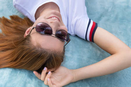 Portrait of young teenage girl in sunglasses laying down on blue cloth background.の写真素材