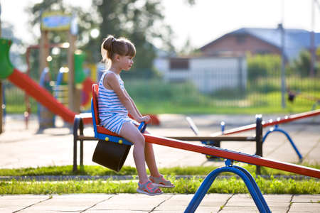 Cute young child girl outdoors on see-saw swing on sunny summer day.の写真素材