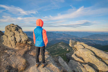 Young child boy hiker standing in mountains enjoying view of amazing mountain landscape.の写真素材