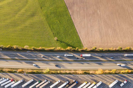 Top down aerial view of highway interstate road with fast moving traffic and parking lot with parked...