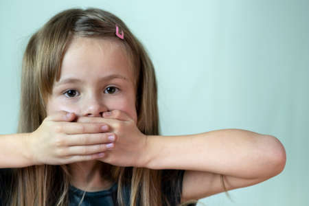 Close-up portrait of little child girl with long hair covering her mouth with hands.の写真素材