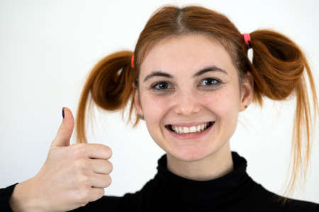 Closeup portrait of a funny redhead teenage girl with childish hairstyle smiling happily isolated on...