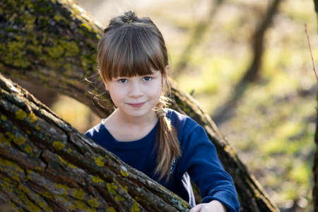 Portrait of a pretty child girl standing near a tree trunk in autumn outdoors.