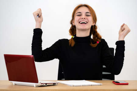 Happy young office worker woman sitting behind working desk with laptop computer, cell phone and notebook.の写真素材