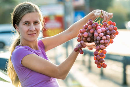 A woman holding big cluster of red juicy grapes in her hand.