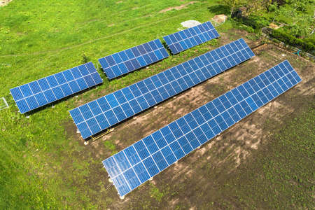 Blue solar photo voltaic panels mounted on metal frame standing on ground with green grass in field.