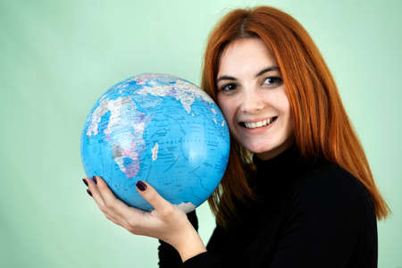 Portrait of a happy young woman holding geographic globe of the world in her hands. Travel...