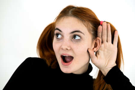 Close up portrait of pretty redhead teenage girl holding a hand to her ear listening to a secret.の写真素材