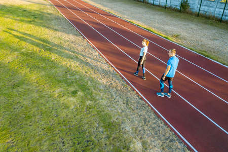 Top down aerial view of two young people sportsman and on red rubber running track of a stadium field resting after jogging marathon in summer.の写真素材