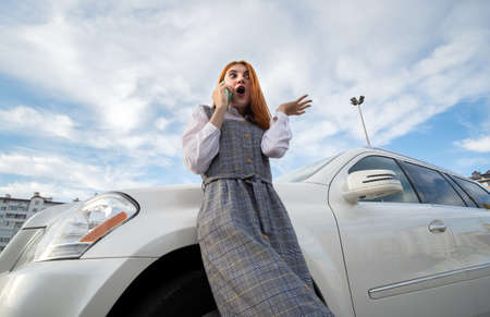 Portrait of a fashionable teenage girl with red hair wearing casual dress standing outside in front...