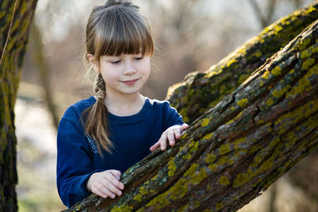 Portrait of a pretty child girl standing near a tree trunk in autumn outdoors.の写真素材