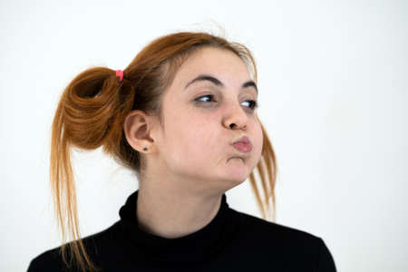 Closeup portrait of a funny redhead teenage girl with childish hairstyle isolated on white...