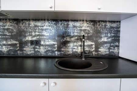 Interior of modern spacious kitchen with white contemporary furniture, black ceramic tiles on the...