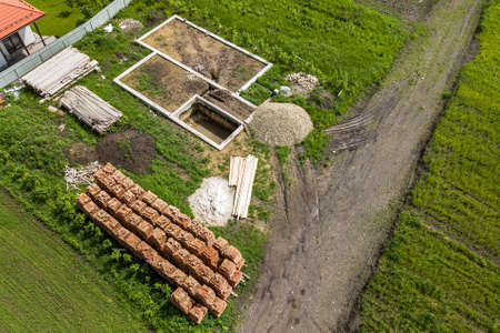 Aerial view of building site for future brick house, concrete foundation floor and stacks of yellow...