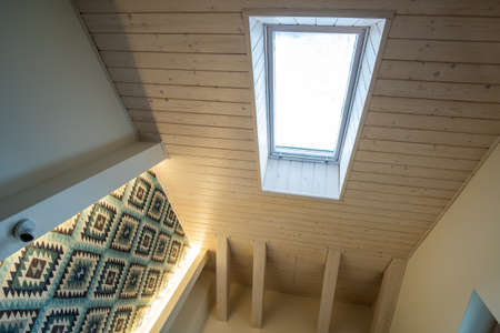 Wooden ceiling in a contemporary mansard room with attic window ob decorative planks surface.の写真素材