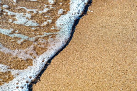 Close up of small sea waves with clear blue water over yellow sand beach at summer sunny shore.の写真素材