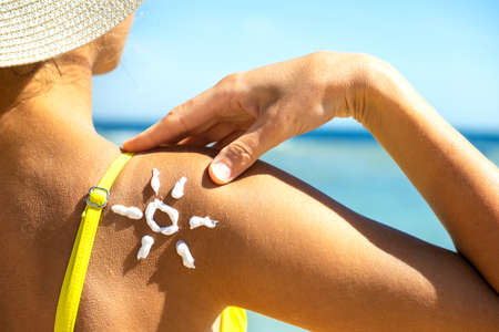 Back view of young woman tanning at the beach with sunscreen cream in sun shape on her shoulder. UV sunburn protection and sunblock skincare conceptの写真素材