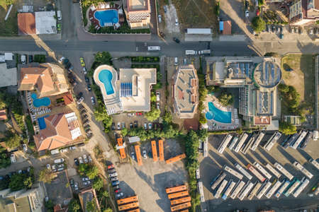 Top down aerial view of hotels roofs, streets with parked cars and swimming pools with blue water in...