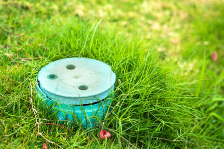 Closeup of green plastic pipe with cover on green grass lawn.