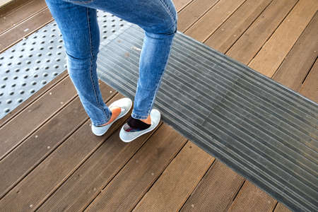 Female legs in denim jeans pants and light summer sneakers standing on wooden floow.の写真素材