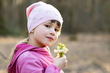 Portrait of happy child girl holding bunch of early spring snowdrops flowers outdoors.の写真素材