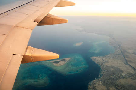 View from airplane on the aircraft white wing flying over ocean landscape in sunny morning. Air travel and transportation concept.の写真素材