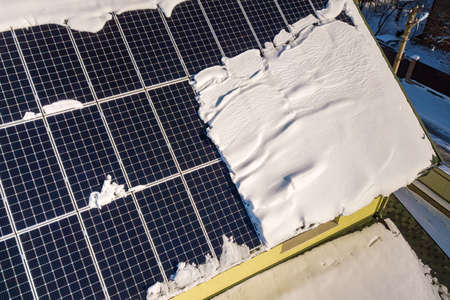 Close up surface of a house roof covered with solar panels in winter with snow on top. Energy...