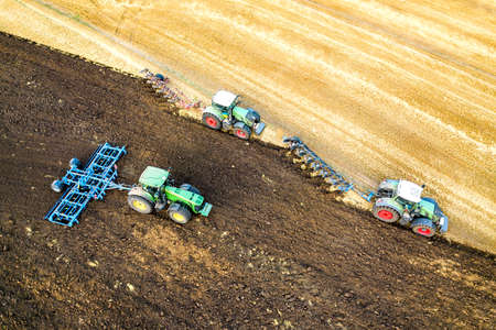 Aerial view of a tractor plowing black agriculture farm field after harvesting in late autumn.の写真素材