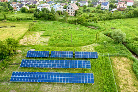 Blue solar photo voltaic panels mounted on metal frame standing on ground with green grass in field.