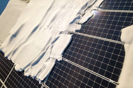Close up surface of a house roof covered with solar panels in winter with snow on top. Energy...