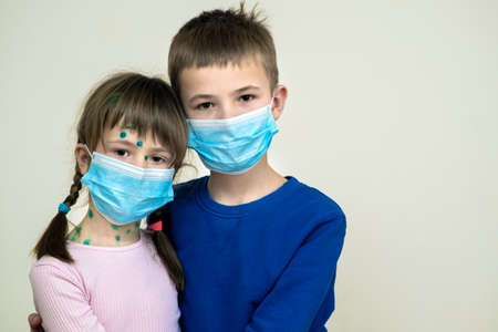 Boy and girl wearing blue protective medical mask ill with chickenpox, measles or rubella virus with...