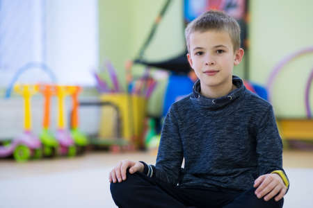 Young child boy sitting and relaxiong on the floor inside sports room in a school after training.の写真素材