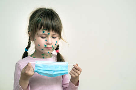 Child girl wearing blue protective medical mask ill with chickenpox, measles or rubella virus with rashes on body. Children protection during epidemic of coronovirus. Covid-19 contagion concept.の写真素材