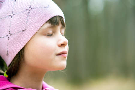 Portrait of young pretty child girl wearing pink jacket and cap enjoying warm sunny day in early...