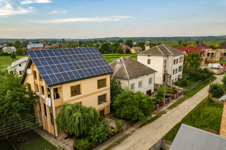 Aerial top view of new modern residential house cottage with blue shiny solar photo voltaic panels system on roof. Renewable ecological green energy production concept.の写真素材