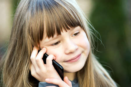 Portrait of pretty child girl with long hair talking on cell phone. Little female kid communicating...