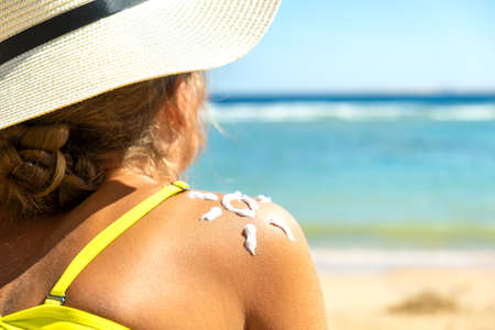 Back view of young woman tanning at the beach with sunscreen cream in sun shape on her shoulder. UV sunburn protection and sunblock skincare conceptの写真素材