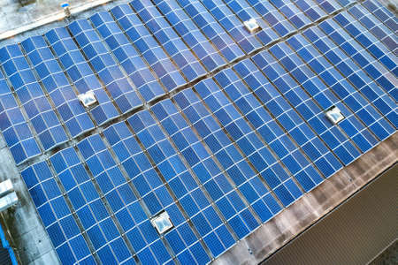 Aerial view of many photo voltaic solar panels mounted of industrial building roof.