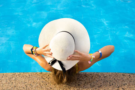 Back view of young woman with long hair wearing yellow straw hat relaxing in warm summer swimming...