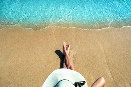 Long slim young woman legs relaxing lying down and sunbathing on sand tropical beach under hot sun in summer. Skincare, sun aging protection and sea travel concept.の写真素材