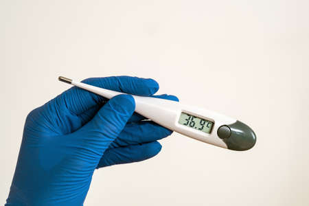Doctor hands in blue protective gloves holding medical thermometer showing slightly high temperature.の写真素材