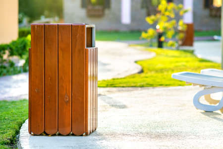 Yellow wooden trash can outdoors on the side of sidewalk in park. Garbage container on street...