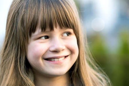 Portrait of pretty child girl with gray eyes and long fair hair smiling outdoors on blurred green...