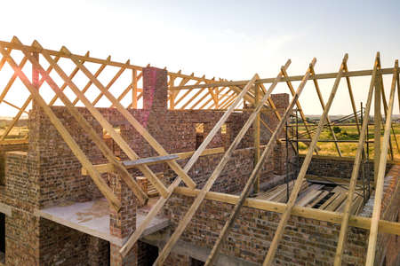 Unfinished brick house with wooden roof structure under construction.