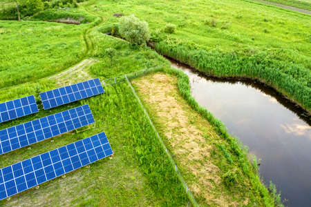 Blue solar photo voltaic panels mounted on metal frame standing on ground with green grass in field.
